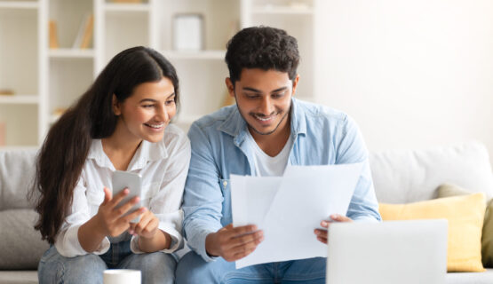 Young Indian couple reviewing document, with laptop and coffee